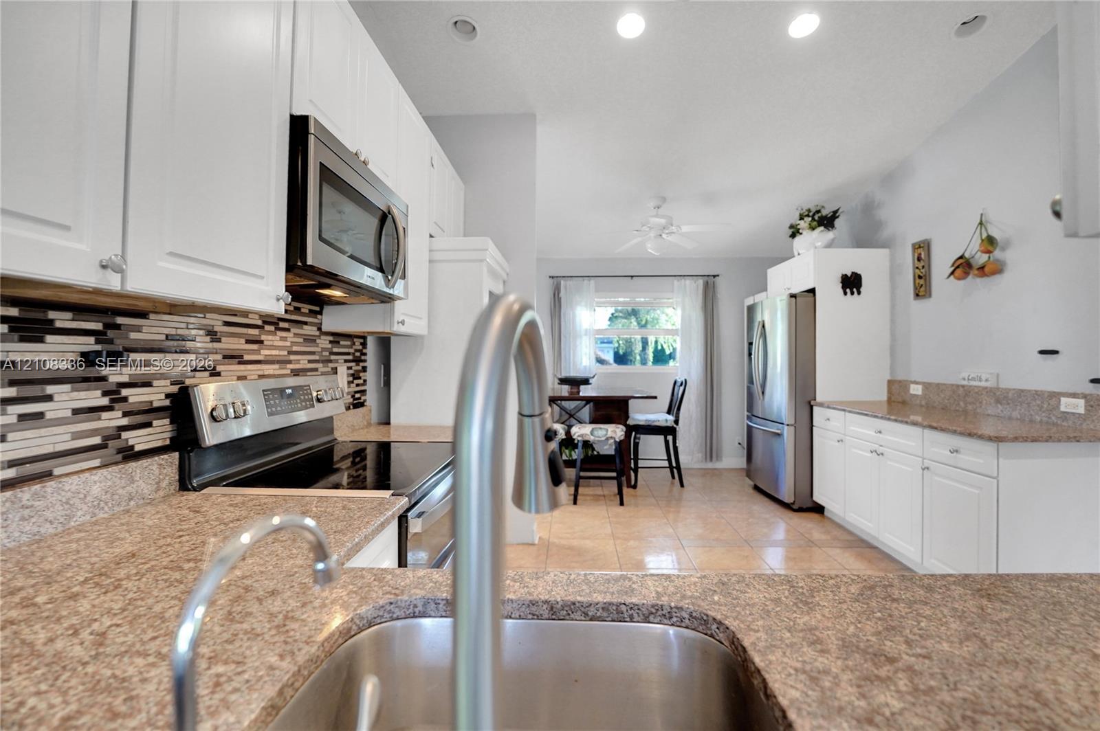 Kitchen featuring white cabinetry, stone-finish countertops, stainless steel appliances, a multi-tone tile backsplash, and tile flooring
