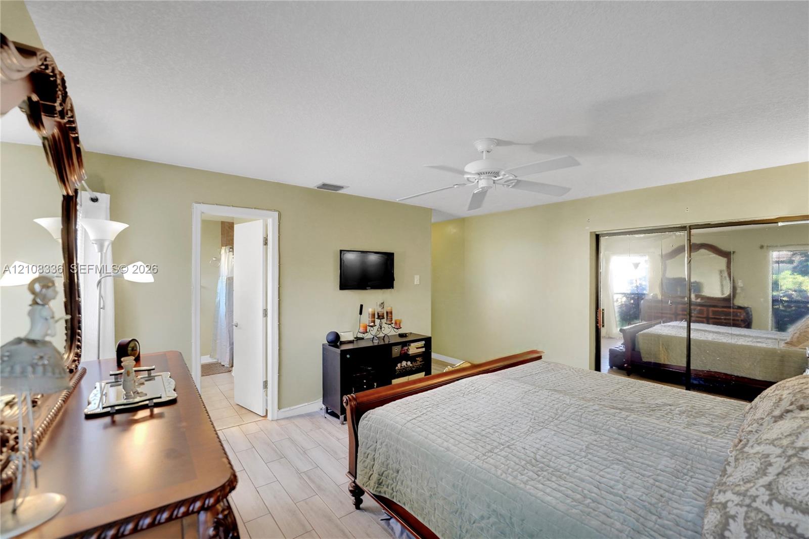 Neutral-toned bedroom featuring wood-finish tile flooring, ceiling fan, and sliding mirrored closet doors