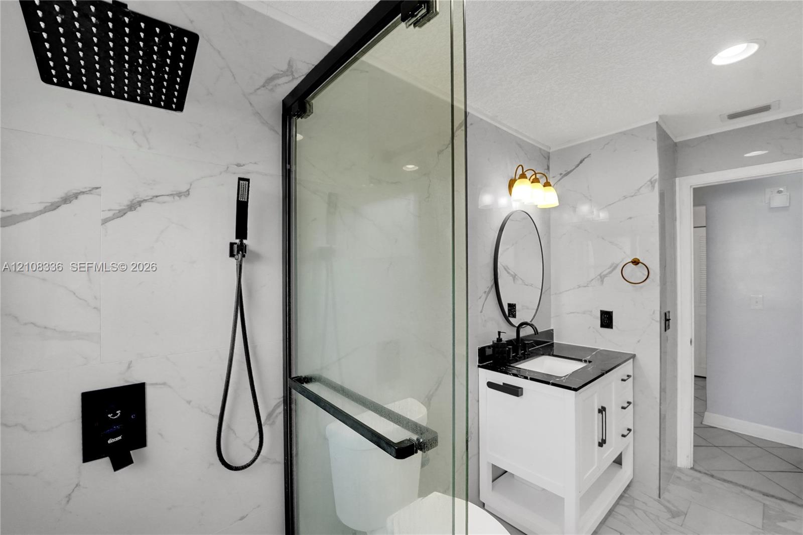 Walk-in shower featuring floor-to-ceiling stone-pattern tile, a rainfall showerhead with handheld attachment, and a black-framed glass enclosure