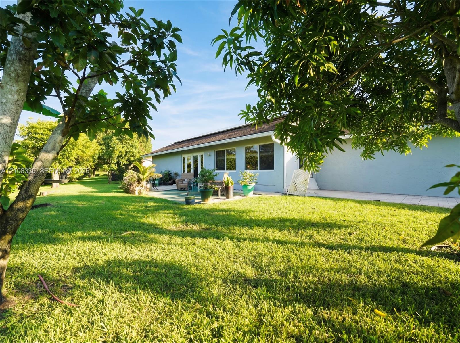 Expansive backyard featuring a sprawling lawn, mature trees, and a paved patio area