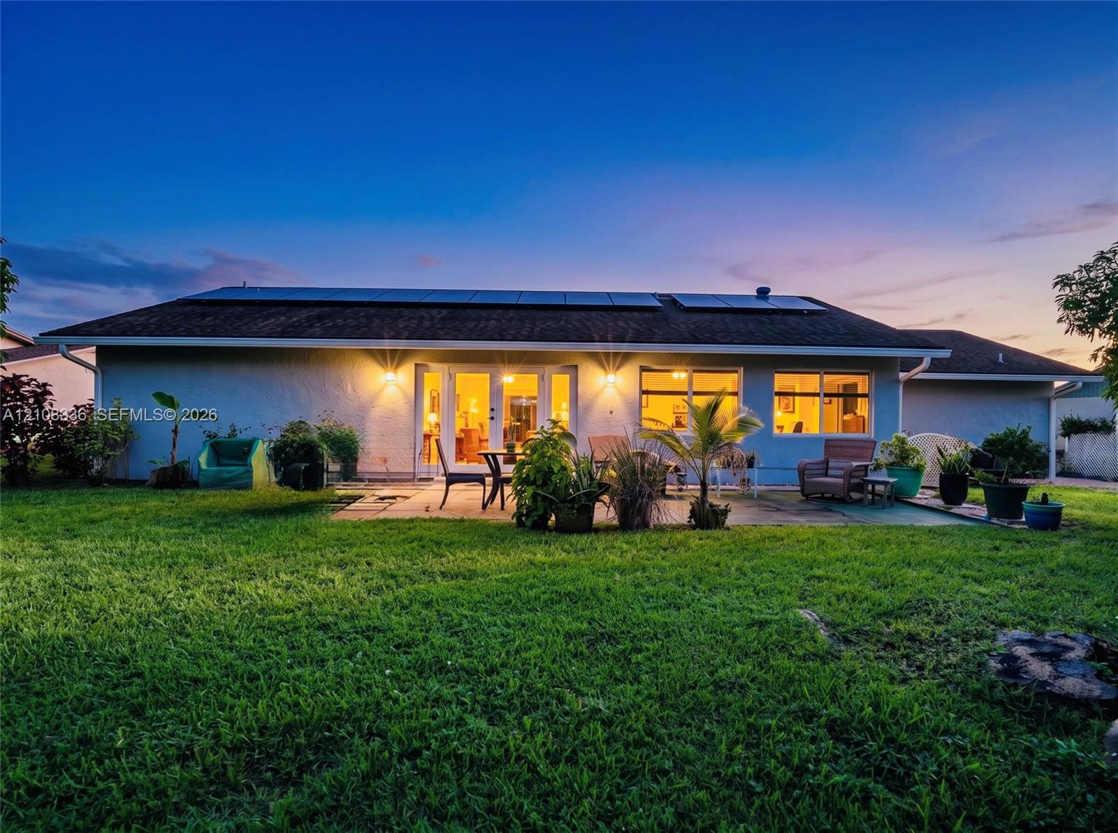 Single-story exterior featuring a concrete patio, roof-mounted solar panels, and large glass French doors