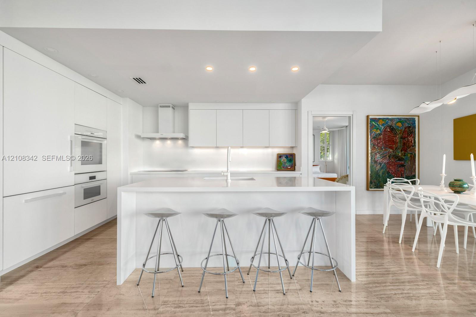 Modern kitchen featuring white flat-panel cabinetry, a central island with a solid-surface countertop, built-in double ovens, and polished stone flooring