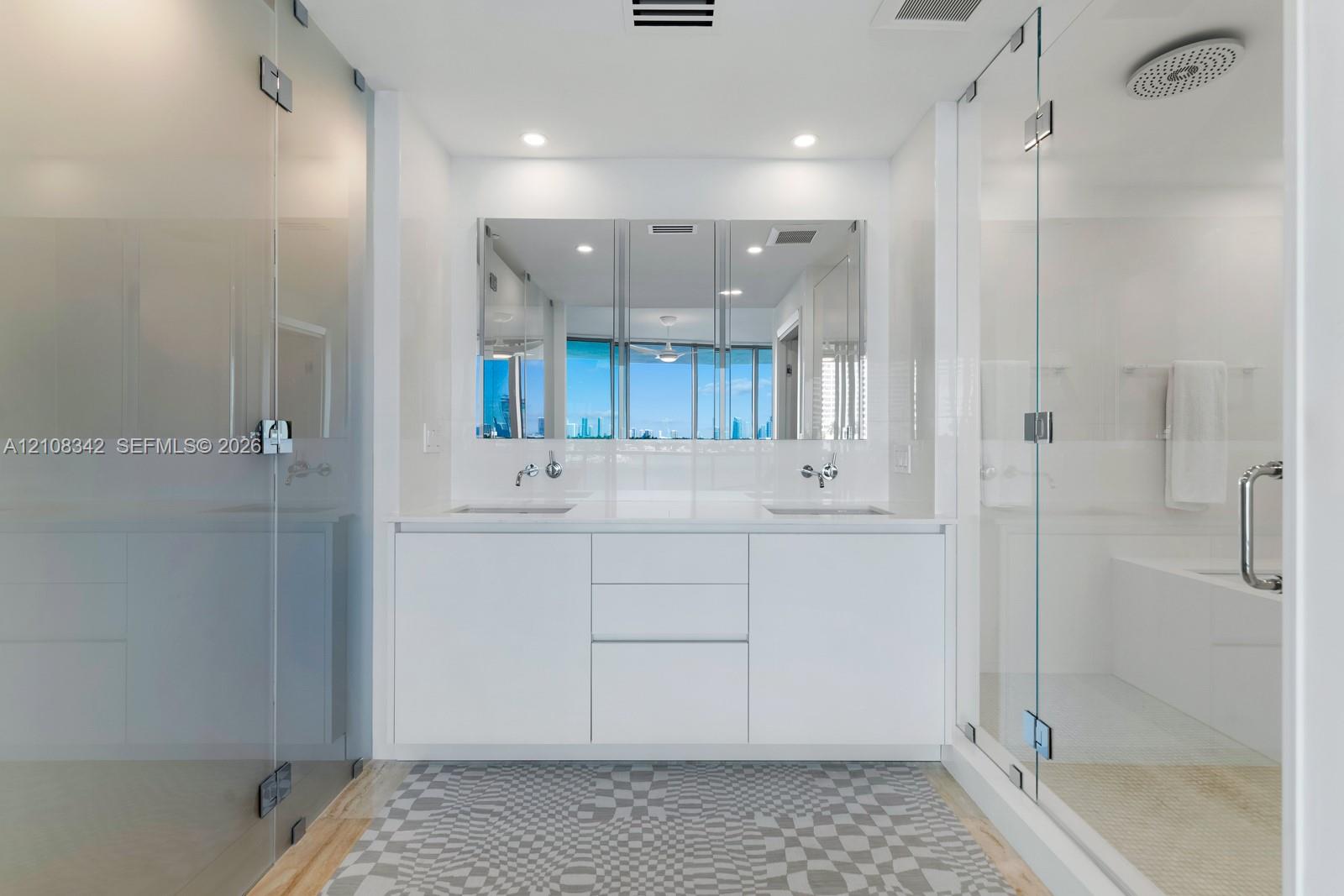 Double vanity with white cabinetry, integrated sinks, wall-mounted faucets, expansive mirrored medicine cabinet, and glass-enclosed shower with rainfall showerhead