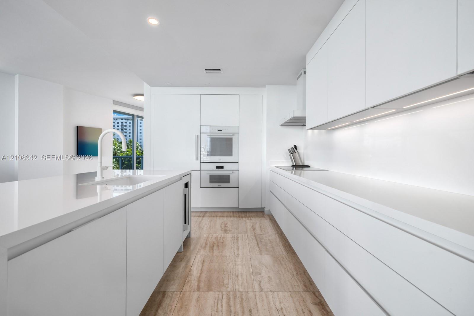 Minimalist kitchen featuring flat-panel cabinetry, white stone-surface countertops, built-in wall ovens, stone-finish flooring, and recessed ceiling lighting