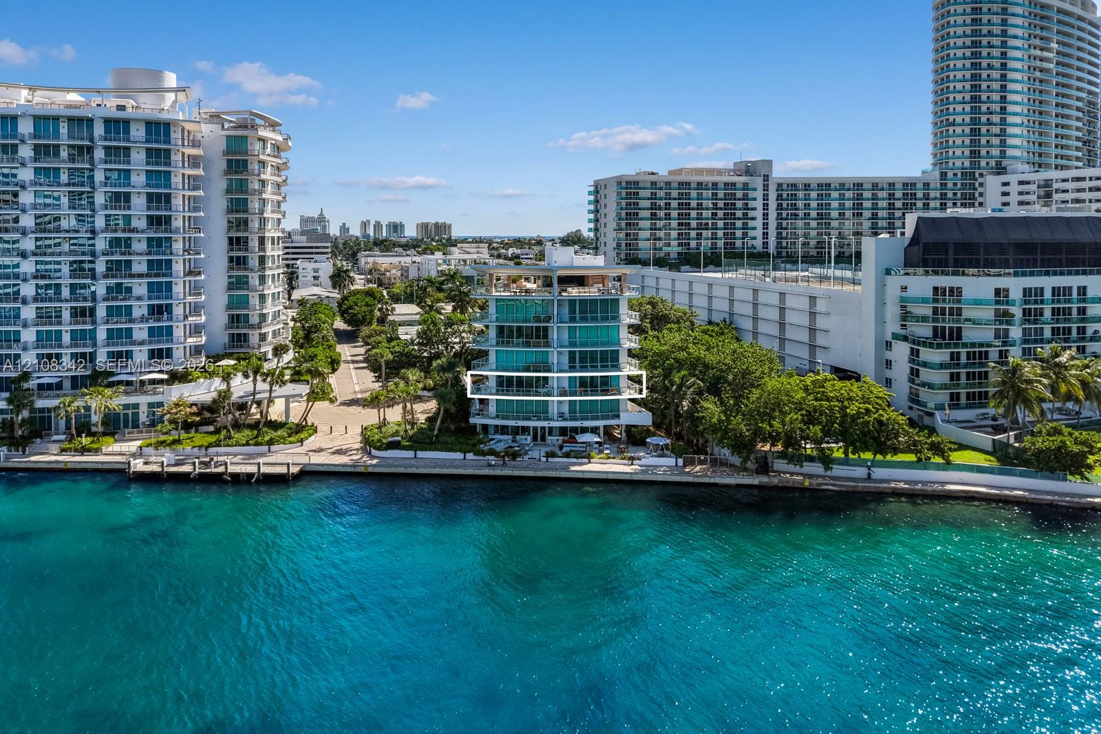 Waterfront mid-rise building featuring floor-to-ceiling glass windows, exterior balconies with glass railings, and concrete bulkhead