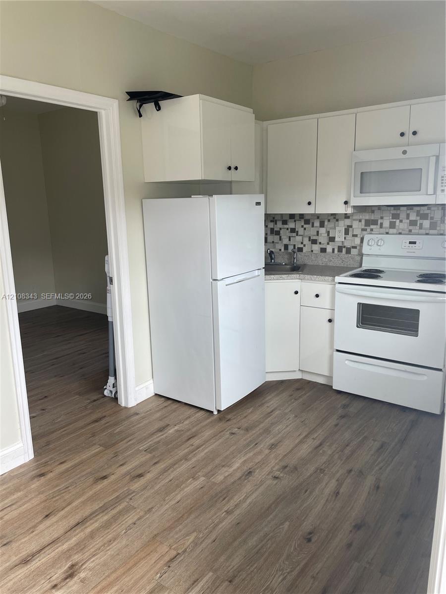 Kitchen featuring white cabinetry, wood-finish flooring, multi-tonal mosaic tile backsplash, and white built-in appliances