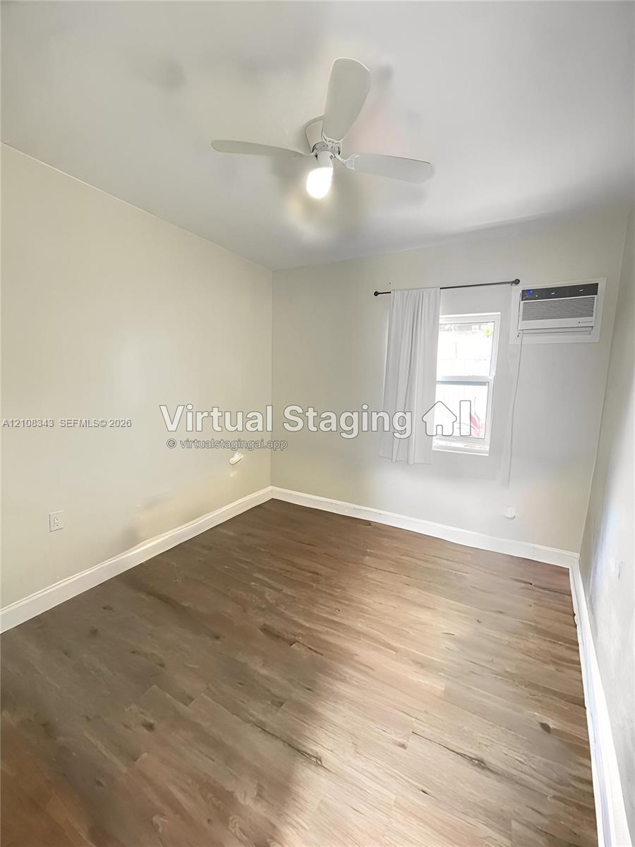 Room featuring wood-finish flooring, a white ceiling fan with integrated lighting, and a wall-mounted air conditioning unit