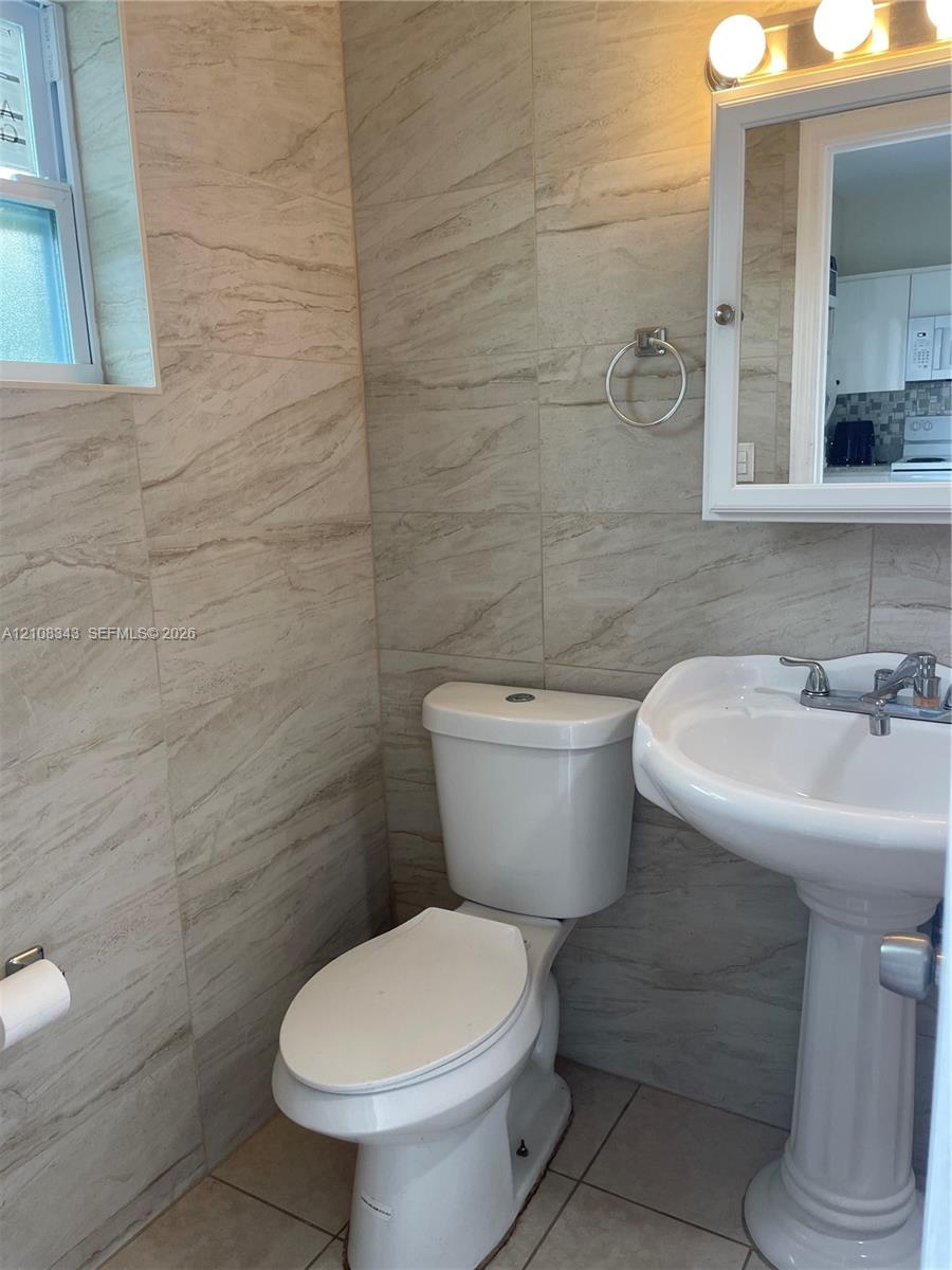 Full-height stone-finish wall tile, white pedestal sink, polished chrome faucet, wall-mounted medicine cabinet, and three-bulb vanity lighting