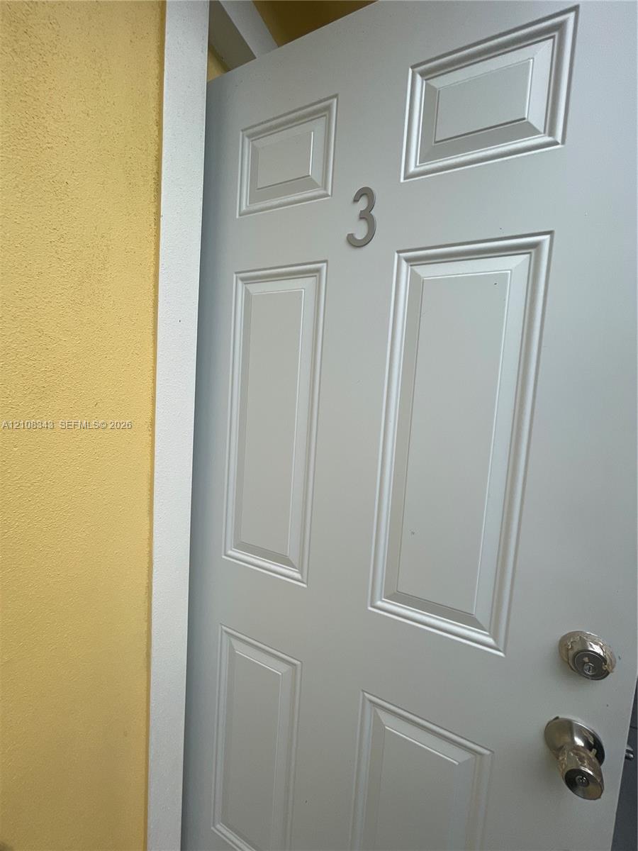 Panelled door featuring a metallic numeral, polished hardware, and a white casing against a stucco wall