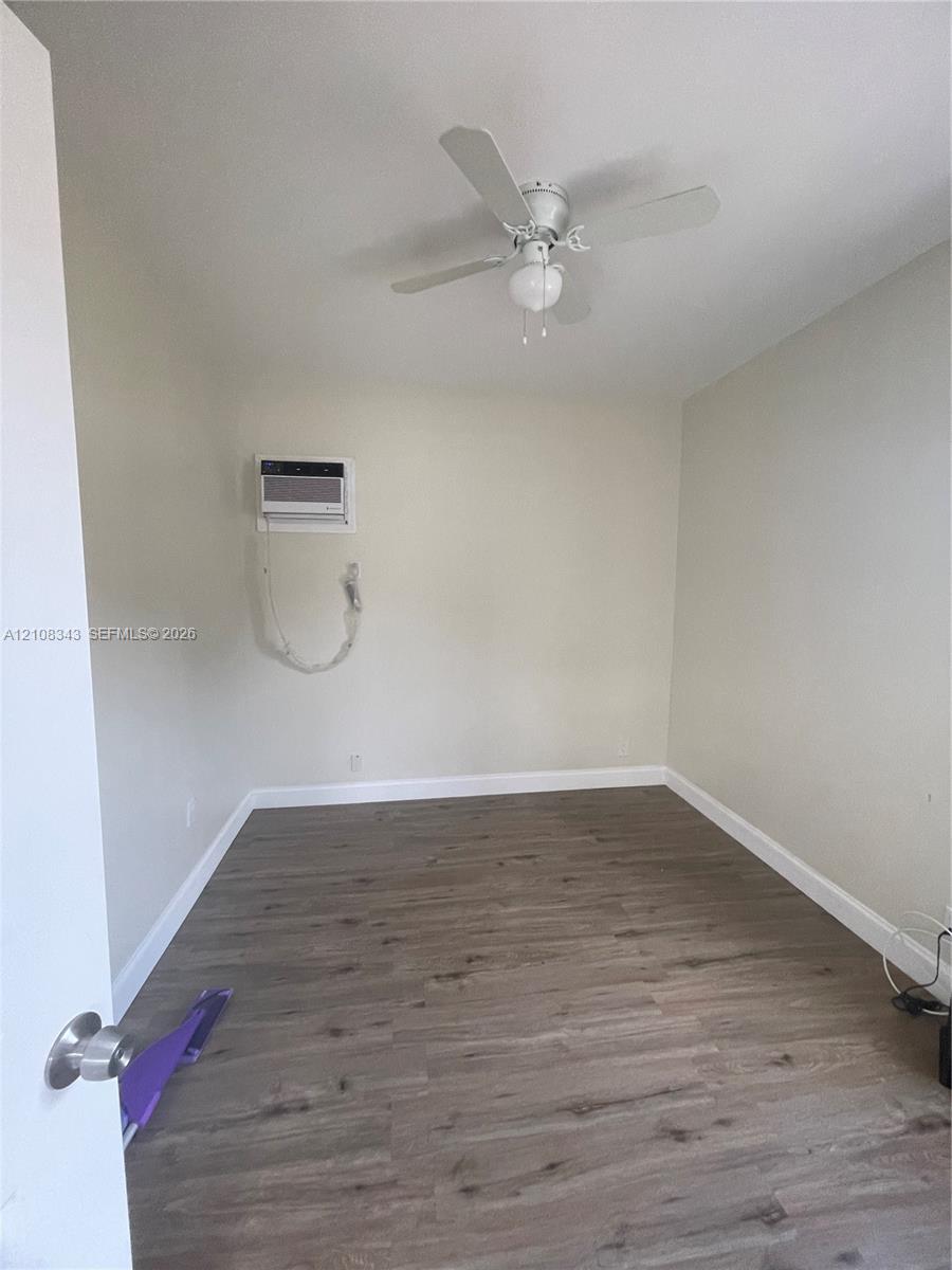 Room featuring wood-finish flooring, a white ceiling fan with integrated lighting, and a wall-mounted air conditioning unit