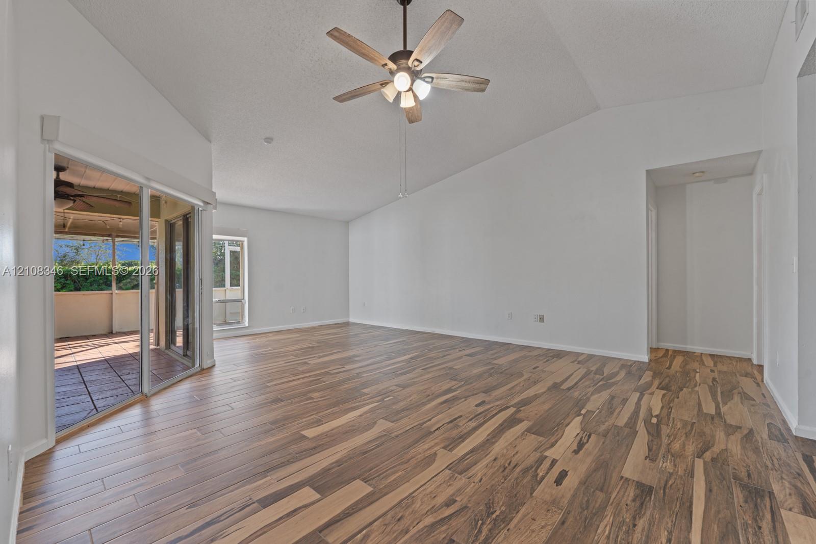 Vaulted ceilings, wood-finish flooring, ceiling fan with integrated lighting, and sliding glass doors Vaulted ceilings, wood-finish flooring, ceiling fan with integrated lighting, and sliding glass doors