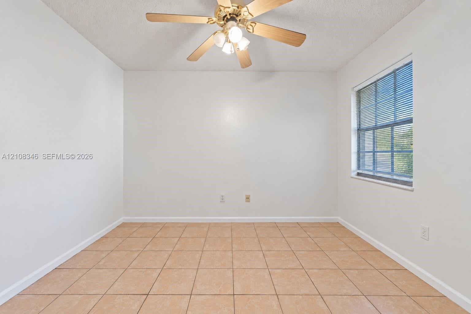 Neutral-toned square tile flooring, light-filled interior with single-pane window, and ceiling-mounted fan with integrated light fixture