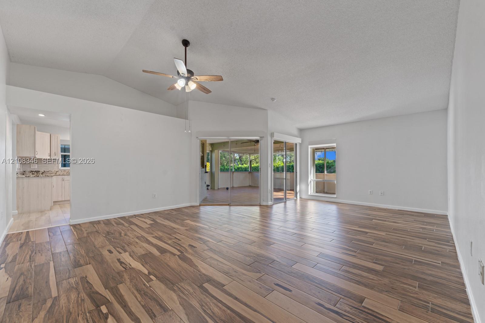 Living area featuring vaulted ceilings, wood-finish tile flooring, a ceiling fan with integrated lighting, and glass sliding doors Living area featuring vaulted ceilings, wood-finish tile flooring, a ceiling fan with integrated lighting, and glass sliding doors