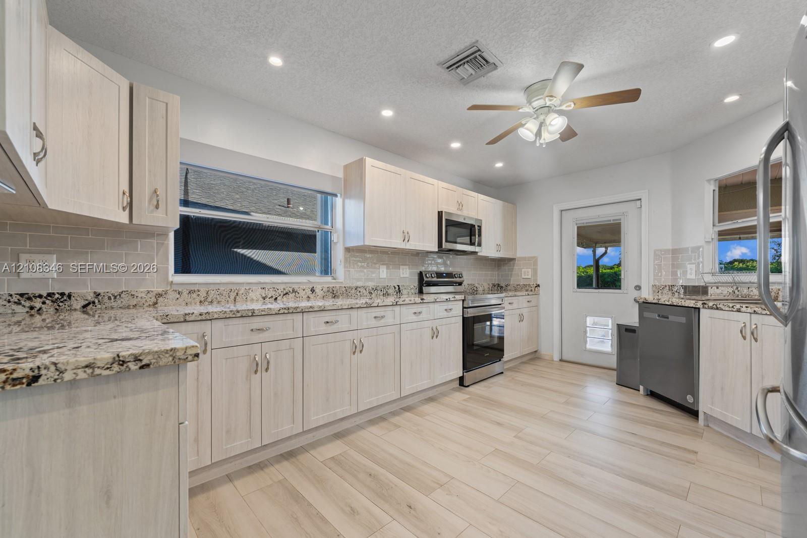 Kitchen featuring light-toned cabinetry, stone countertops, subway tile backsplash, stainless steel appliances, and wood-tile flooring Kitchen featuring light-toned cabinetry, stone countertops, subway tile backsplash, stainless steel appliances, and wood-tile flooring