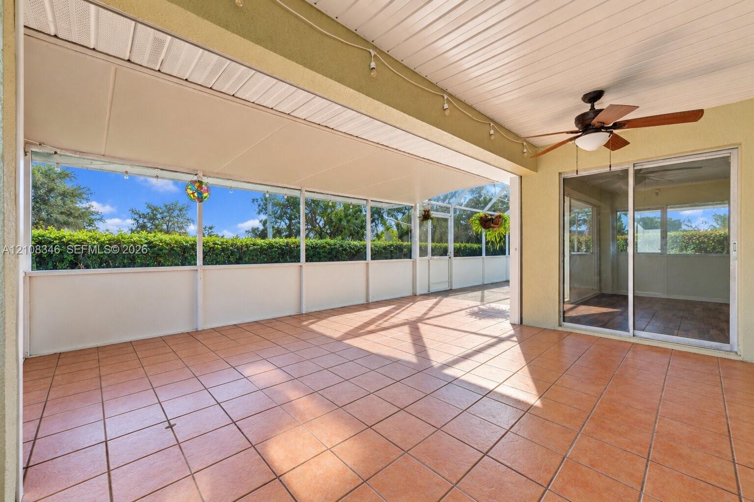 Screened-in lanai featuring ceramic tile flooring, a white paneled ceiling, a ceiling fan, and sliding glass door access