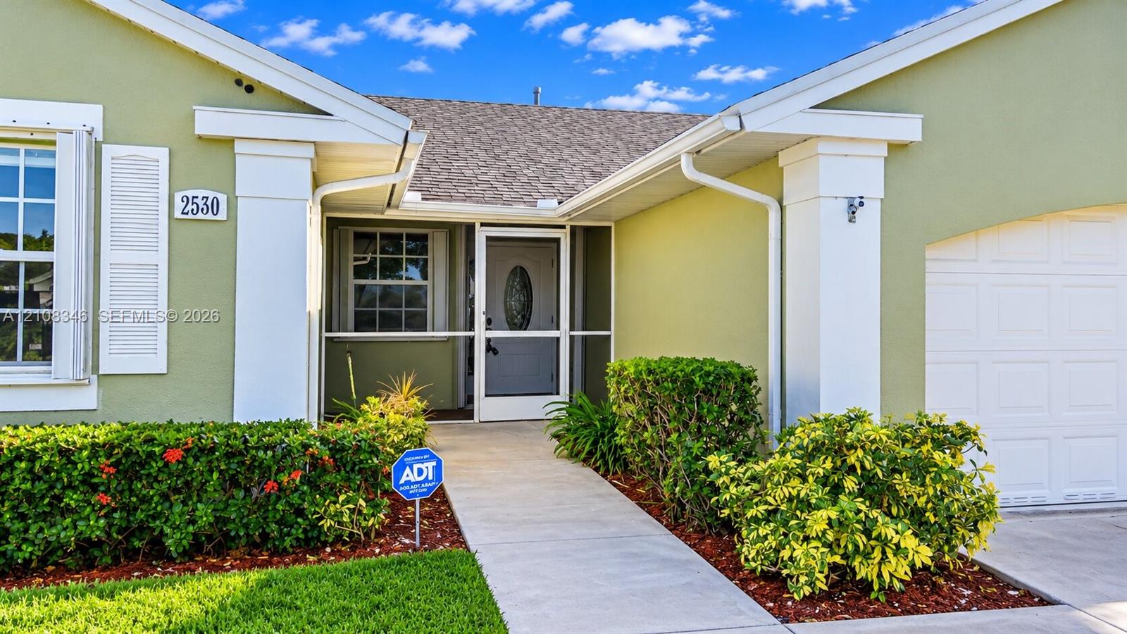 Stucco exterior featuring decorative shutters, a covered entryway with a screened storm door, a concrete walkway, and an attached garage