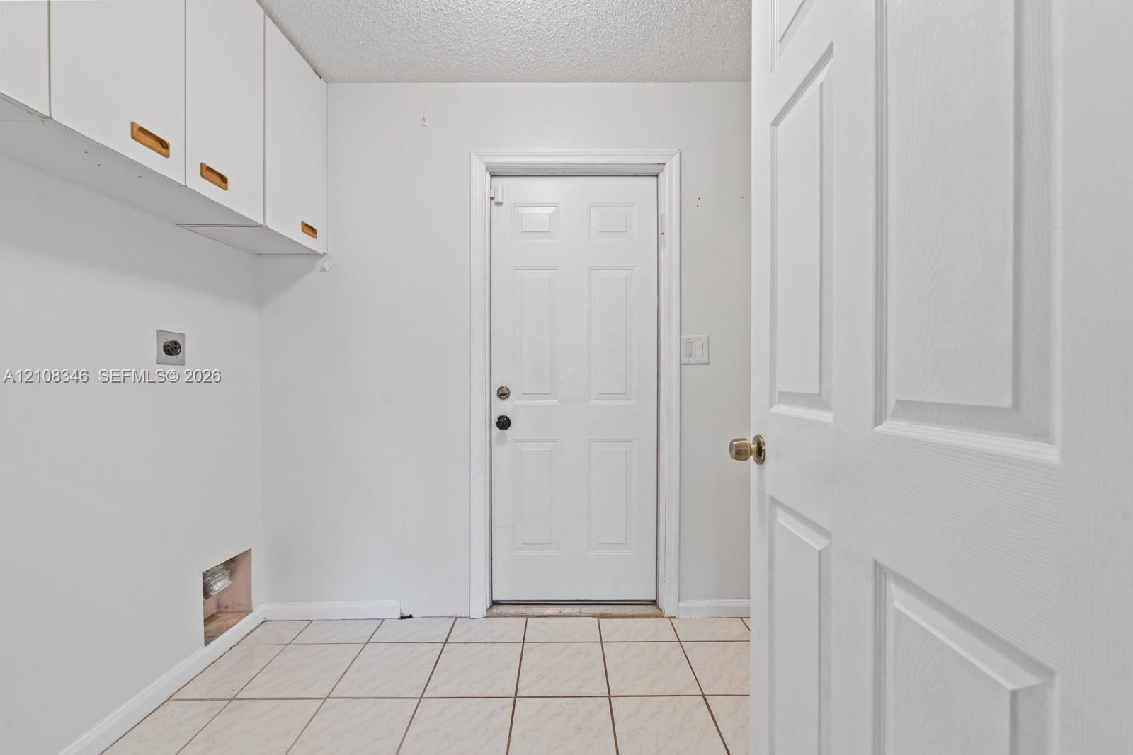 Utility space featuring white wall-mounted cabinetry, tile flooring, and a six-panel exterior door