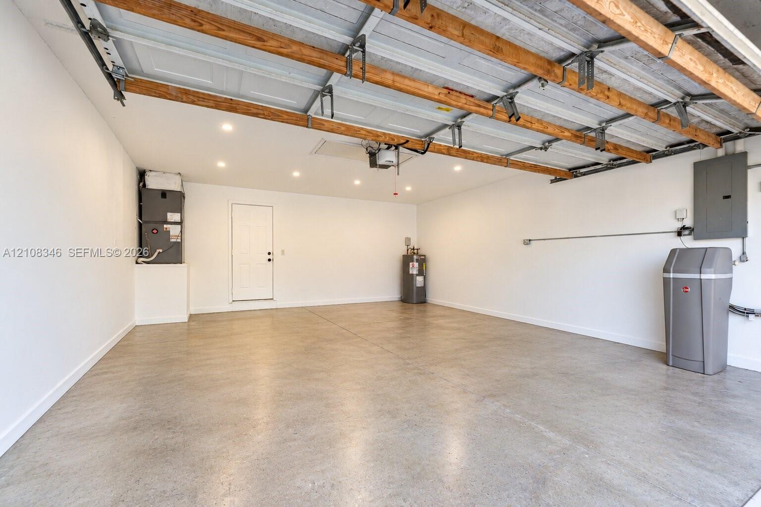 Spacious garage featuring concrete flooring, recessed lighting, exposed wood ceiling rafters, a dedicated water heater, and an integrated water softening system