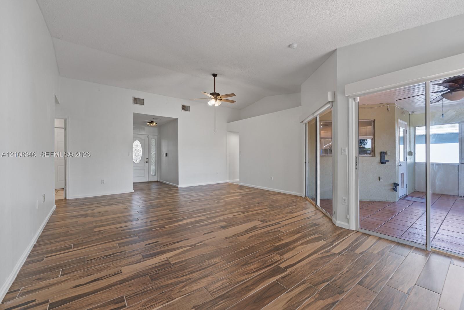 Open floor plan featuring vaulted ceilings, wood-finish tile flooring, ceiling fan with integrated lighting, and glass sliding doors Open floor plan featuring vaulted ceilings, wood-finish tile flooring, ceiling fan with integrated lighting, and glass sliding doors
