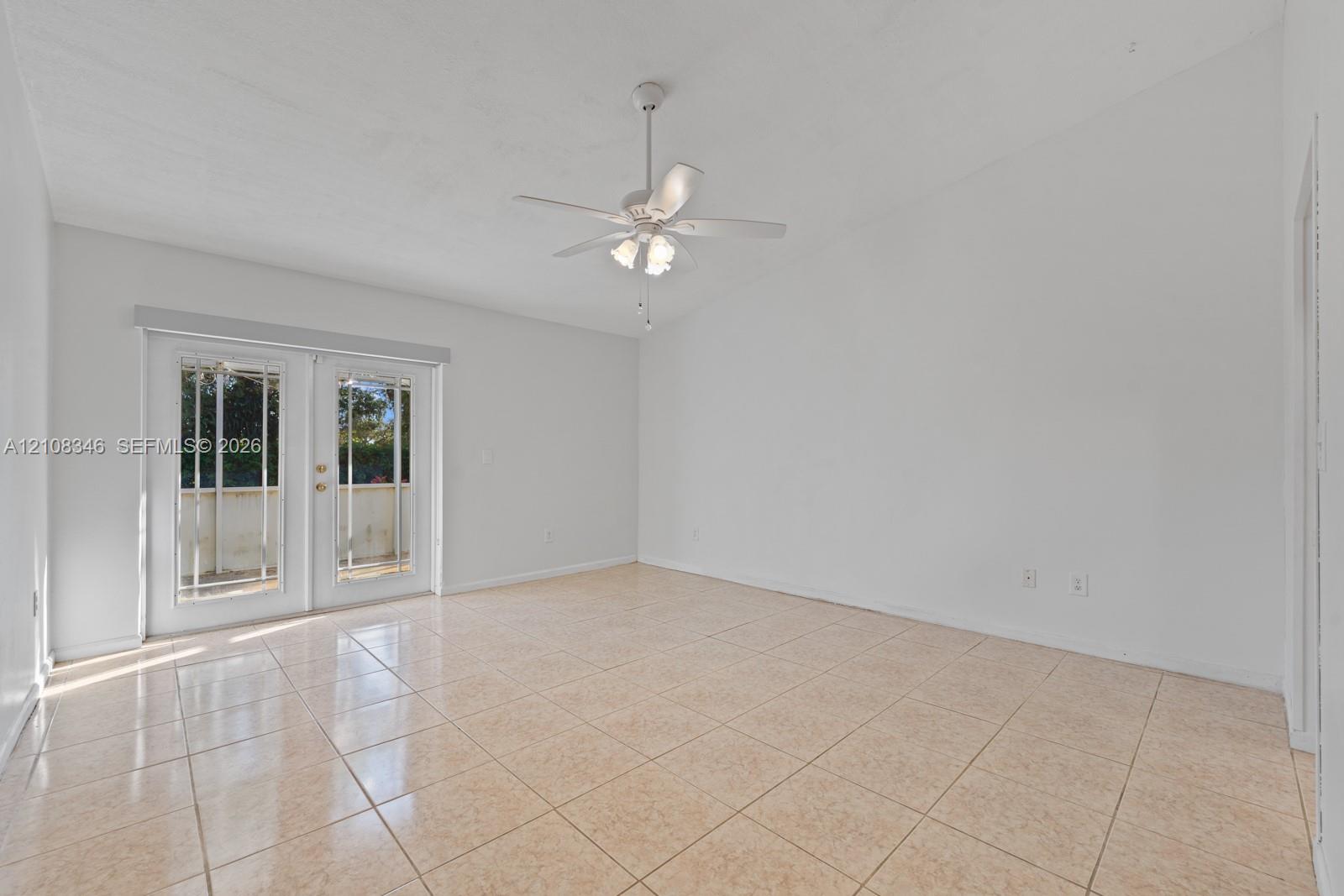 Spacious interior featuring neutral ceramic tile flooring, vaulted ceilings, a white ceiling fan with integrated lighting, and full-glass French doors Spacious interior featuring neutral ceramic tile flooring, vaulted ceilings, a white ceiling fan with integrated lighting, and full-glass French doors