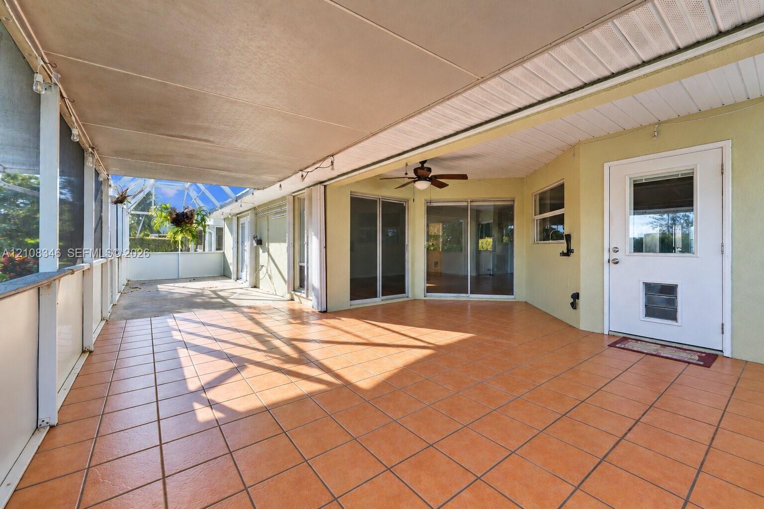 Screened-in lanai featuring ceramic tile flooring, a solid roof cover, a ceiling fan, and sliding glass door entry