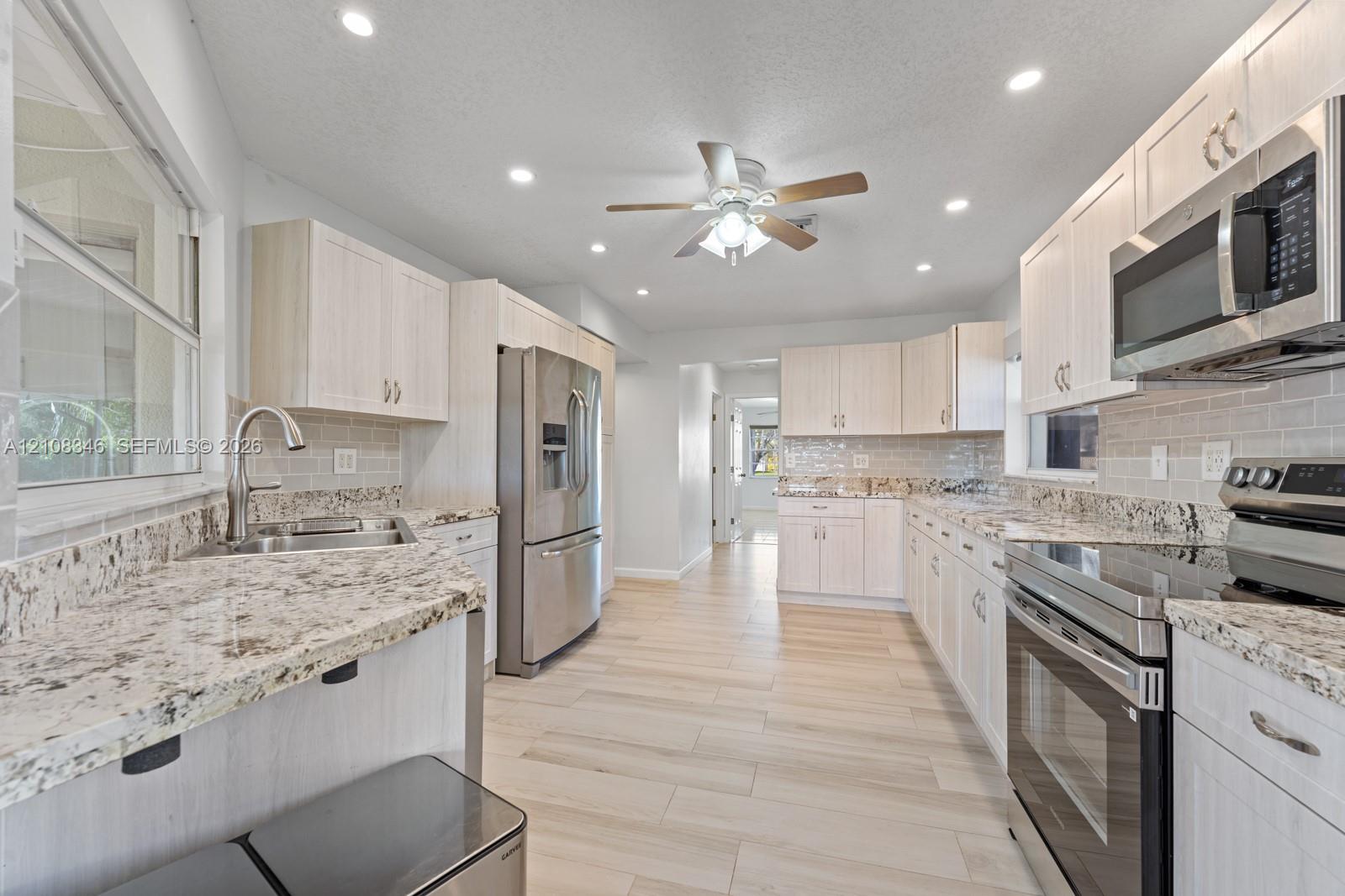 Kitchen featuring light-toned wood cabinetry, stone countertops, stainless steel appliances, subway tile backsplash, and wood-tile flooring Kitchen featuring light-toned wood cabinetry, stone countertops, stainless steel appliances, subway tile backsplash, and wood-tile flooring