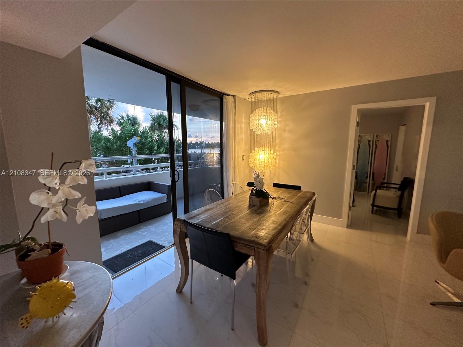 Dining area featuring large-format light-toned flooring, tiered crystal chandelier, and floor-to-ceiling glass sliding doors opening to a covered balcony