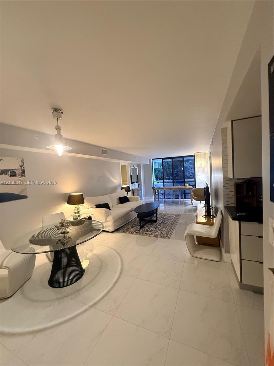 Open-concept floor plan featuring large-format polished tile flooring, recessed ceiling lighting, a contemporary pendant light fixture, and floor-to-ceiling glass sliding doors