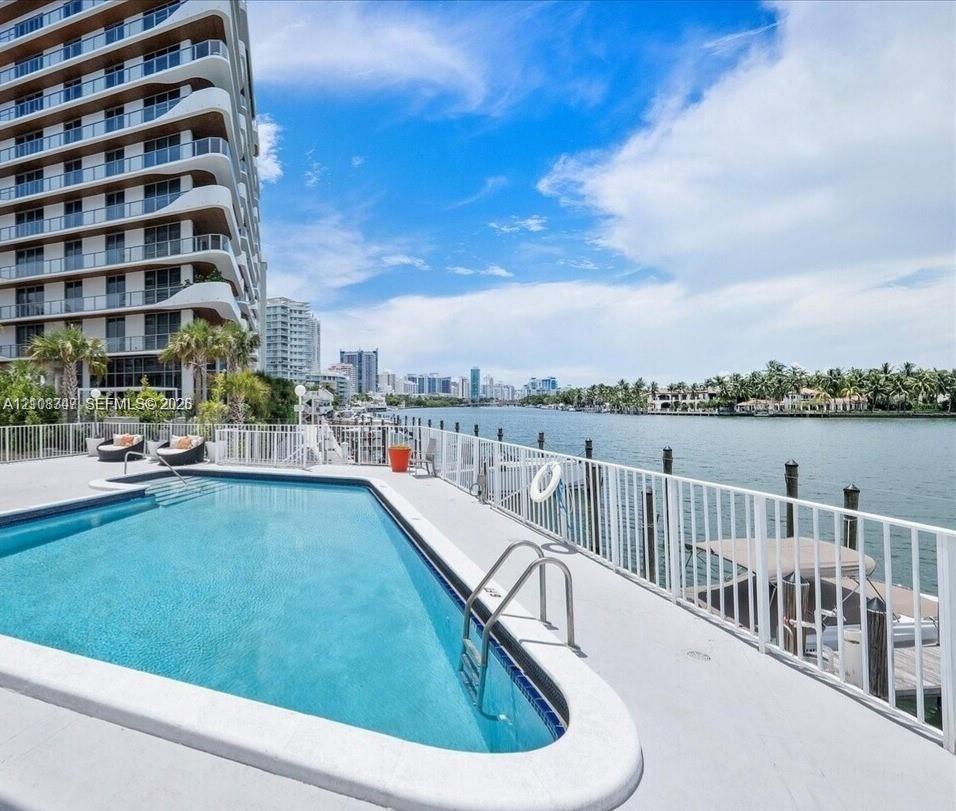 Waterfront swimming pool with concrete decking, perimeter metal fencing, and a private dock