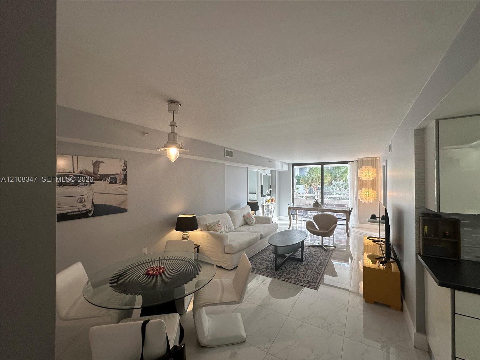 Open-concept living space featuring large-format tile flooring, industrial-style pendant lighting, and floor-to-ceiling glass doors