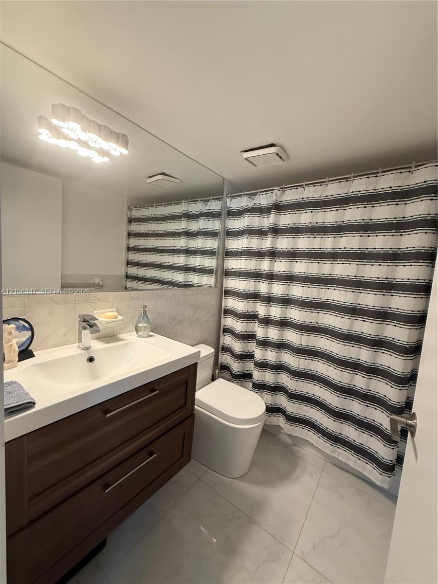 Bathroom featuring a wood-finish vanity with a rectangular sink, wall-spanning mirror, sleek faucet, and large-format tile flooring