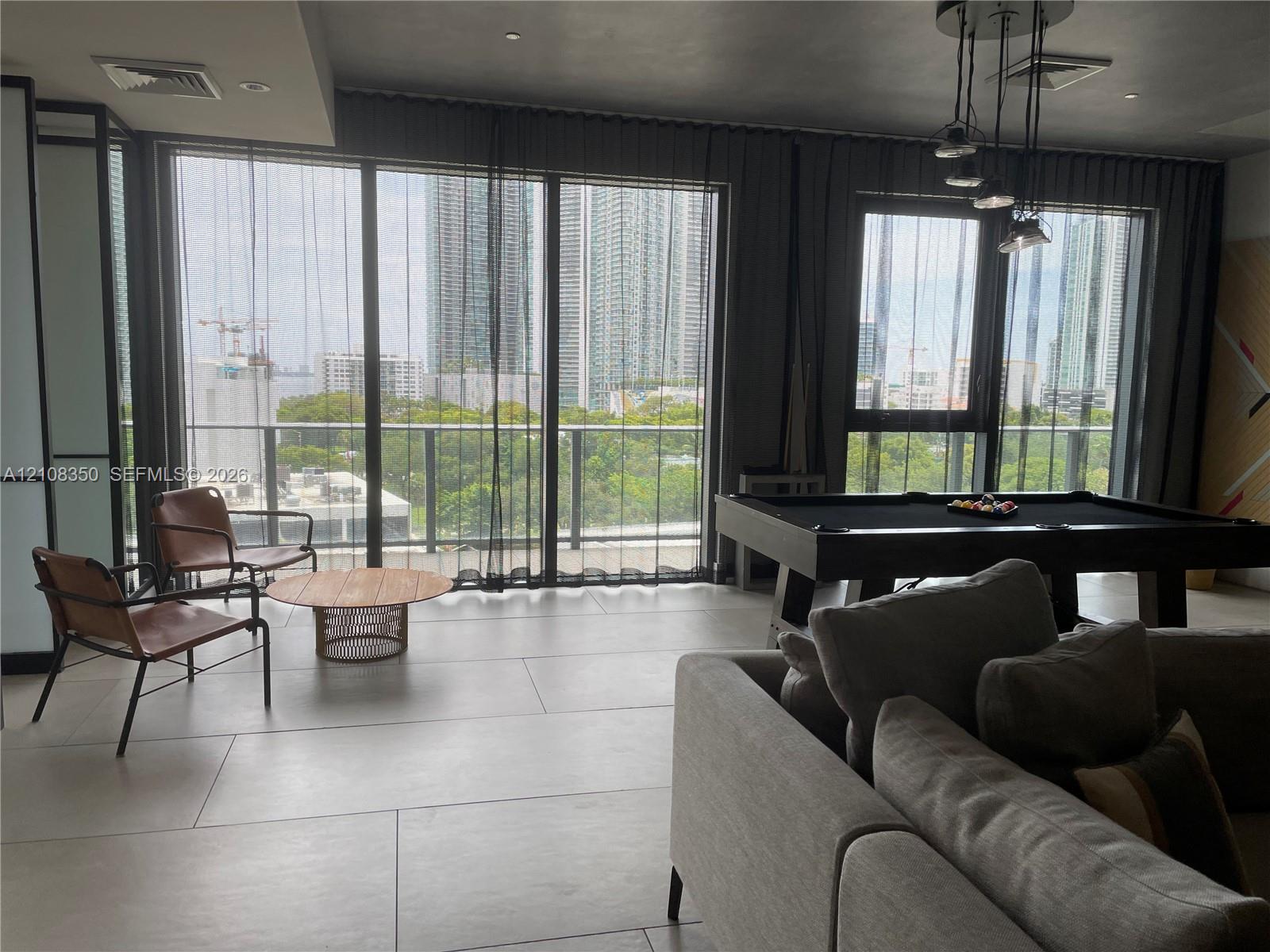Floor-to-ceiling glass panel windows, large-format tile flooring, multi-pendant metal lighting fixture, and a railed balcony