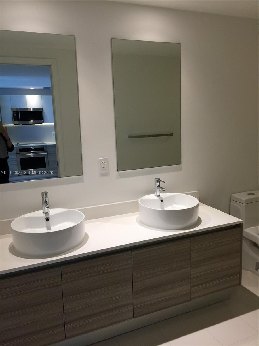 Floating vanity with wood-finish cabinetry, white countertop, dual vessel sinks, chrome faucets, and rectangular wall mirrors