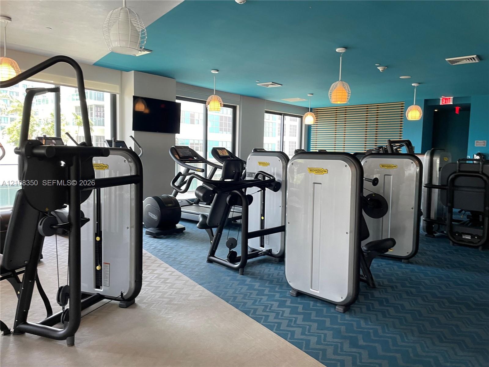 Fitness center featuring a variety of professional-grade exercise equipment, geometric patterned carpet, recessed and pendant lighting, and floor-to-ceiling windows