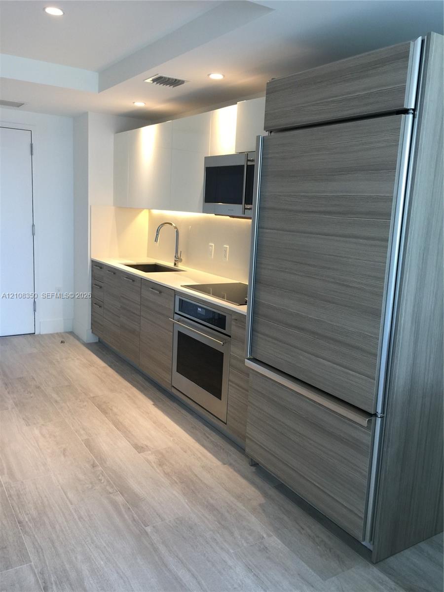 Kitchen featuring flat-panel wood-finish cabinetry, integrated refrigerator, stone countertop, stainless steel oven, and recessed lighting