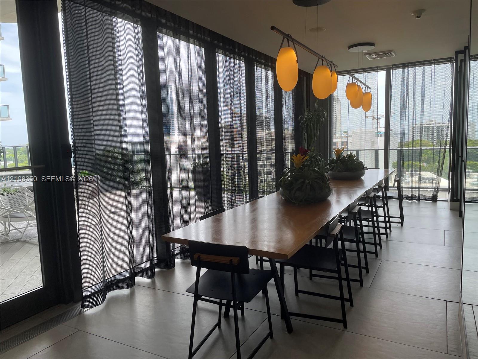Floor-to-ceiling glass paneling with sliding door access to a balcony, large-format tile flooring, and custom multi-pendant lighting fixture