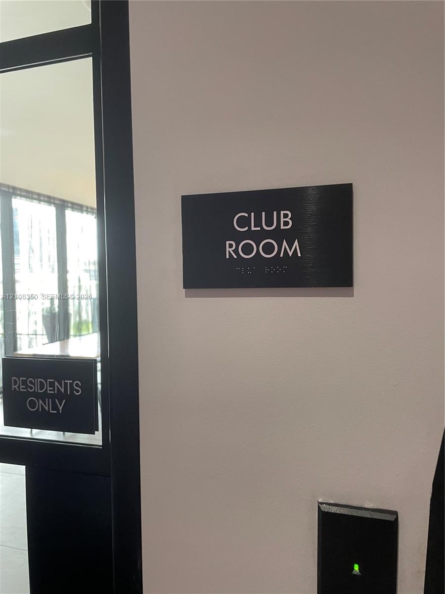 Club room entrance featuring a black signage panel with braille and a secure electronic access control system
