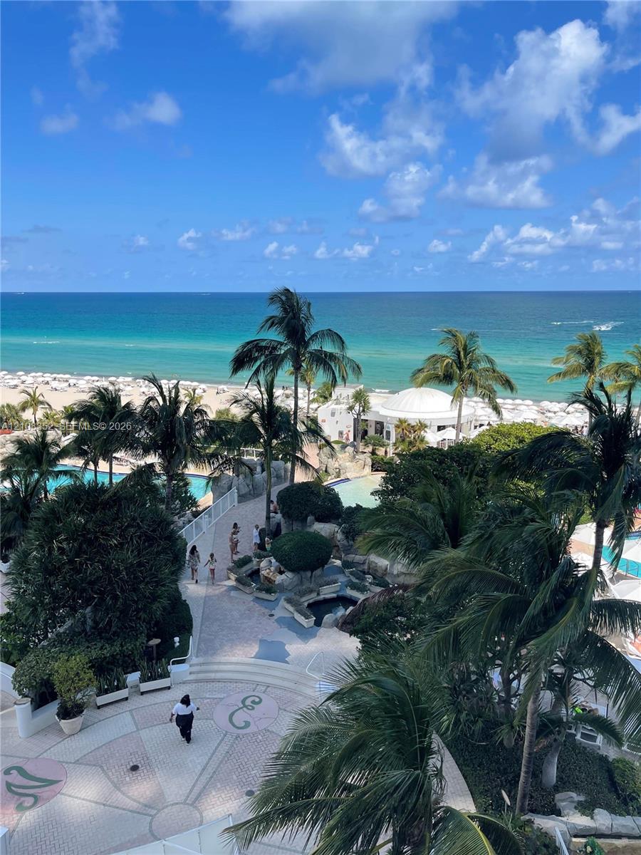 Oceanfront balcony perspective featuring tropical landscaping, expansive resort-style pools, stone-paved walkways, and immediate access to the coastline