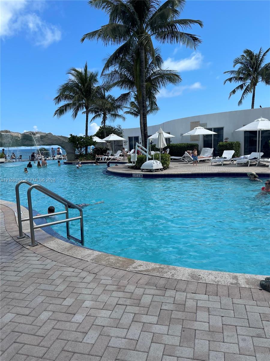Swimming pool with a stone water feature, paved deck, and mature palm trees