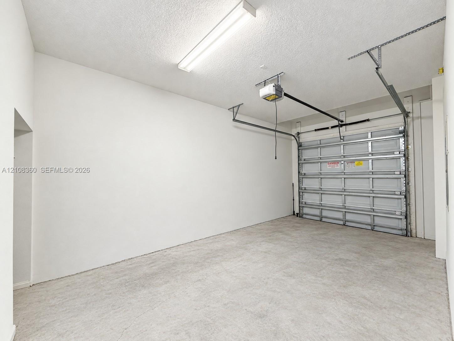 Attached garage featuring a concrete floor, high-clearance ceiling, integrated automatic door opener, and linear fluorescent lighting