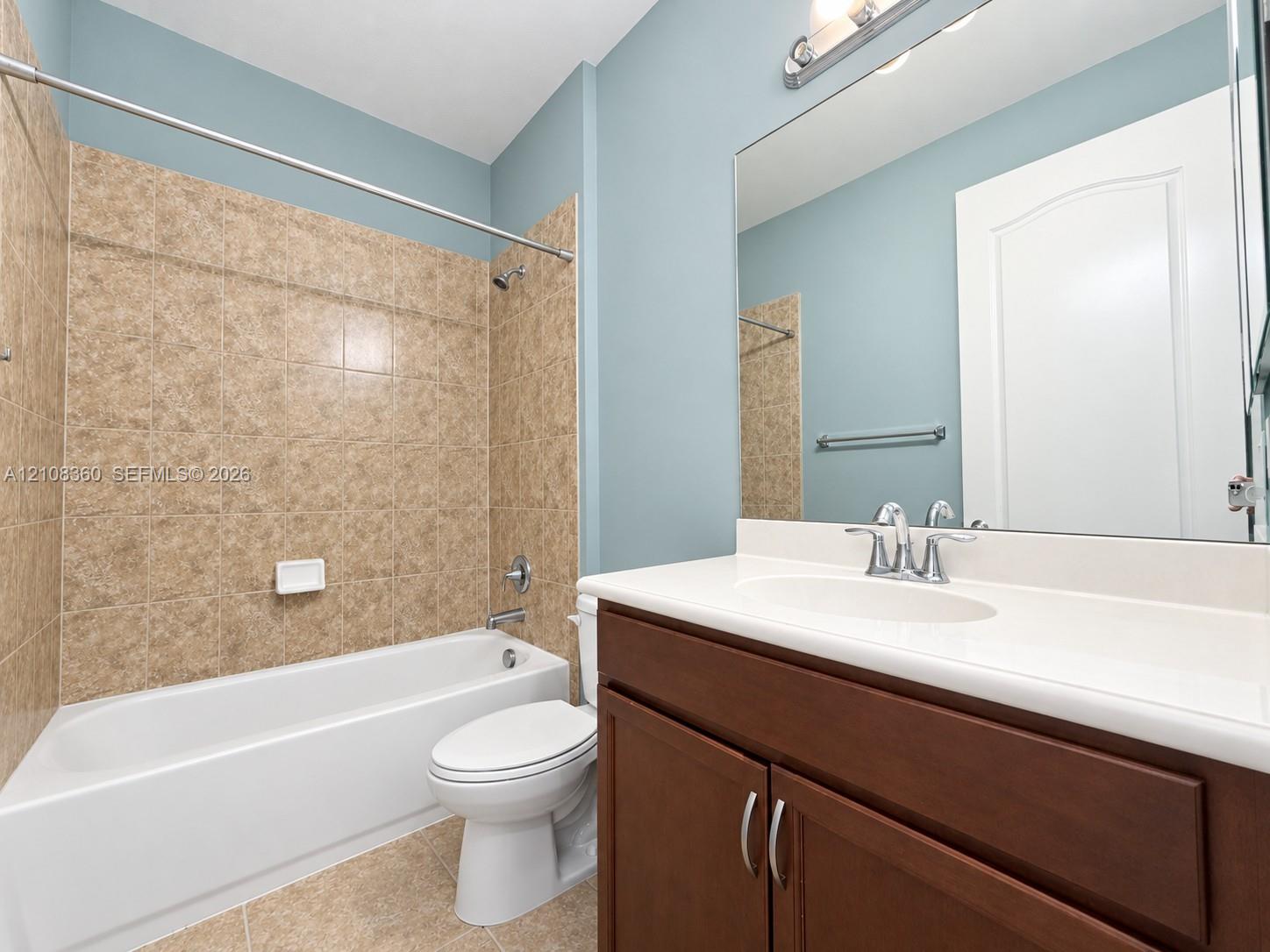 Bathroom featuring a white porcelain tub, wood-finish vanity with a solid-surface countertop, integrated sink, and large wall-mounted mirror