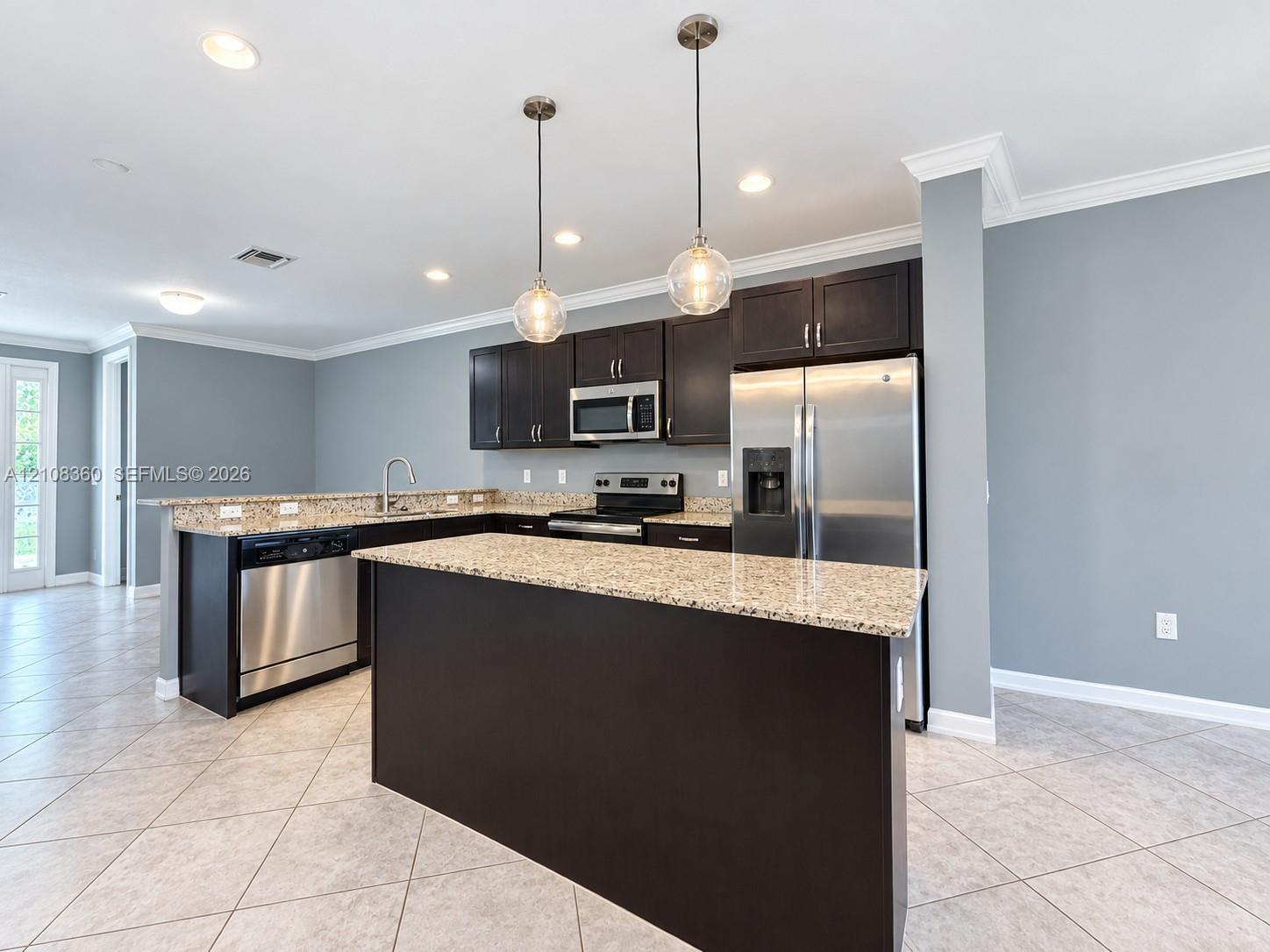 Kitchen featuring dark cabinetry, stone-surface countertops, stainless steel appliances, a central island, and globe pendant lighting Kitchen featuring dark cabinetry, stone-surface countertops, stainless steel appliances, a central island, and globe pendant lighting