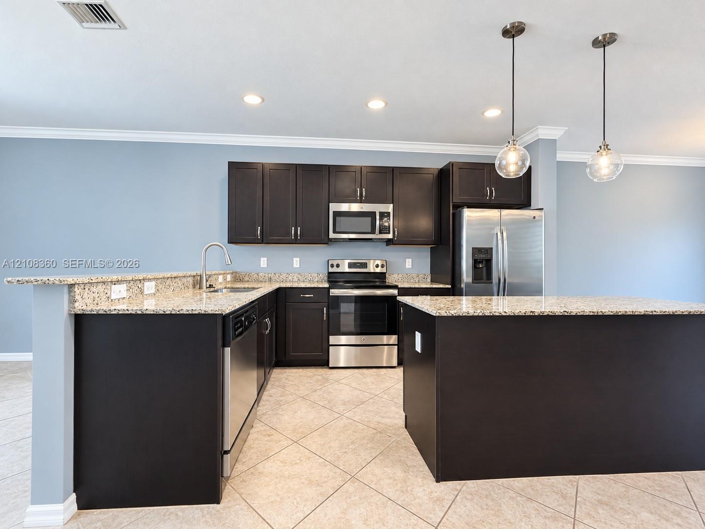 Kitchen featuring dark wood cabinetry, stone countertops, stainless steel appliances, a peninsula island, and globe pendant lighting Kitchen featuring dark wood cabinetry, stone countertops, stainless steel appliances, a peninsula island, and globe pendant lighting