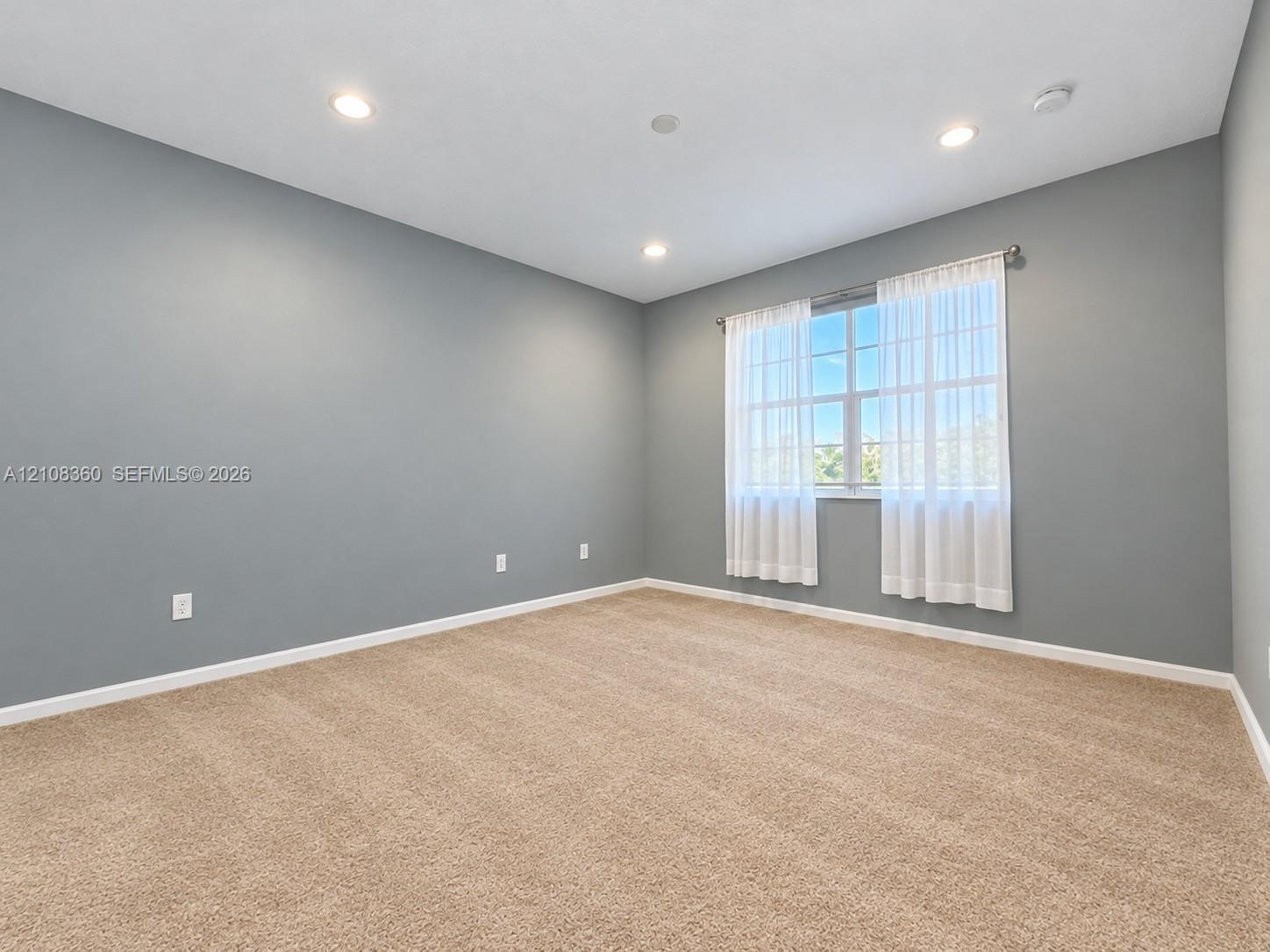 Neutral-toned interior space featuring recessed ceiling lighting, wall-to-wall carpeting, and a multi-pane window
