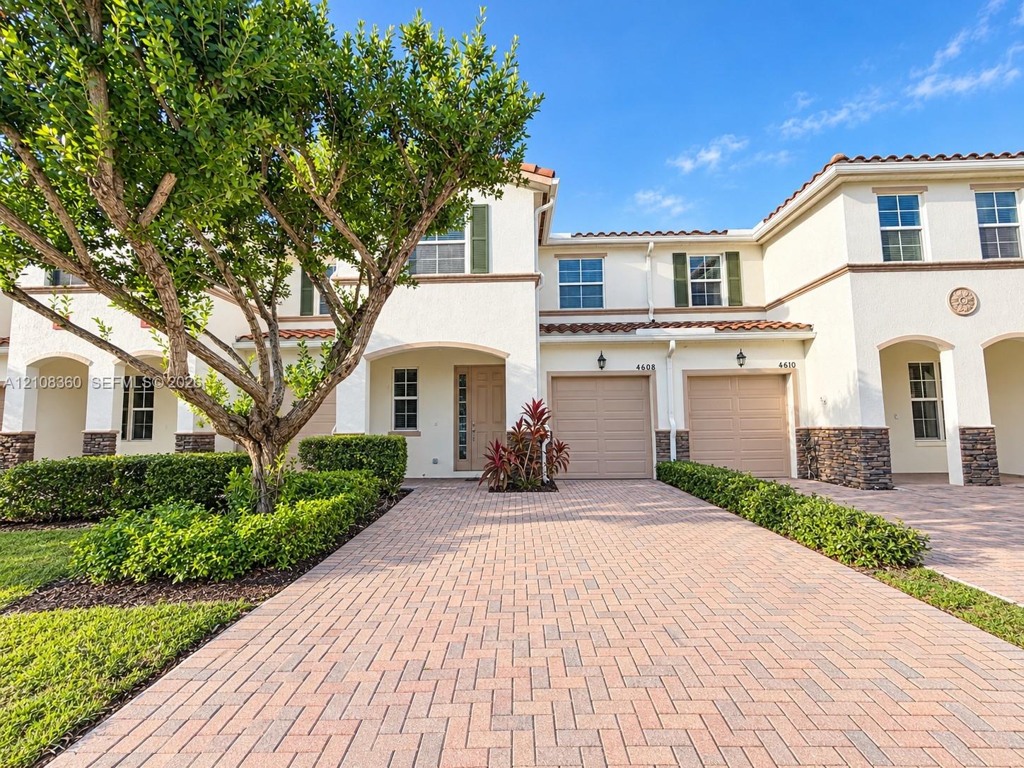 Stucco exterior featuring stone veneer accents, paver driveway, tile roofing, and attached two-car garages