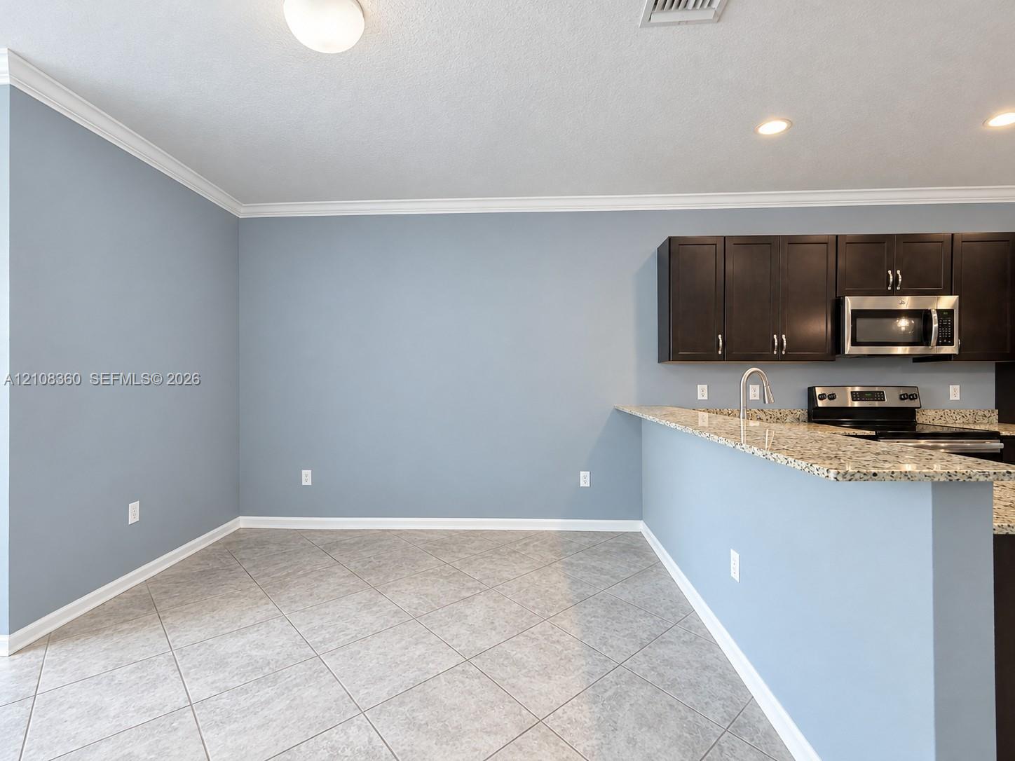 Kitchen area featuring dark cabinetry, speckled stone countertops, stainless steel appliances, tile flooring, and crown molding Kitchen area featuring dark cabinetry, speckled stone countertops, stainless steel appliances, tile flooring, and crown molding