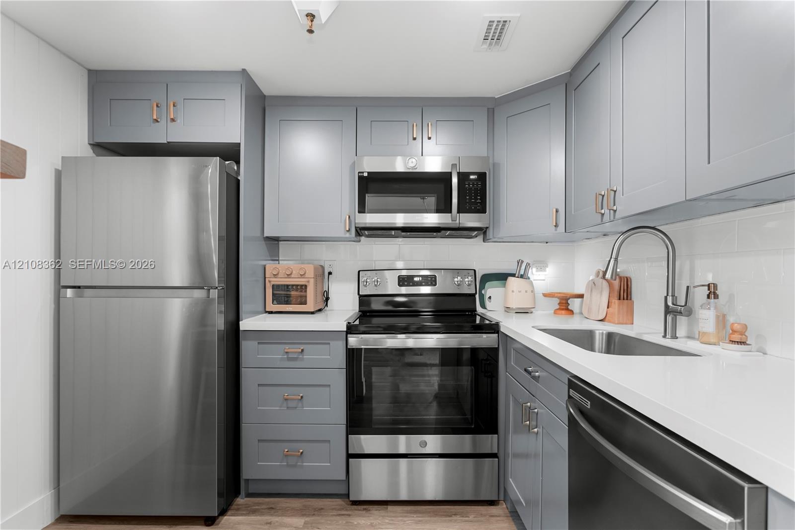 Kitchen featuring shaker-style cabinetry with metallic hardware, white solid-surface countertops, subway tile backsplash, and stainless steel appliances