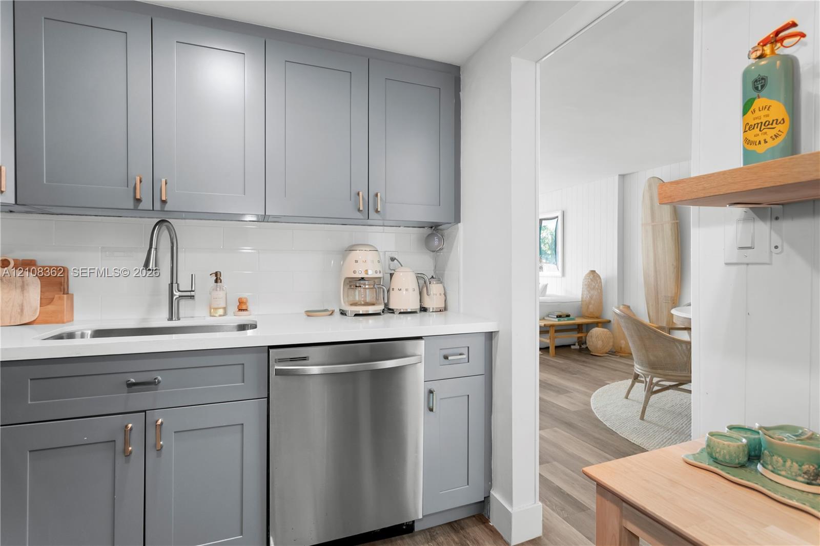 Kitchen featuring grey shaker-style cabinetry, white subway tile backsplash, solid-surface countertops, undermount stainless steel sink with pull-down faucet, and built-in stainless steel dishwasher