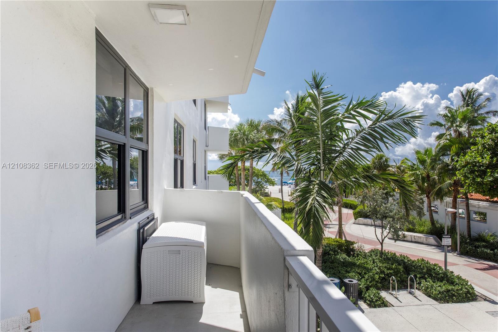 Covered balcony with smooth concrete flooring, solid masonry privacy walls, and metal railings, featuring black-framed windows