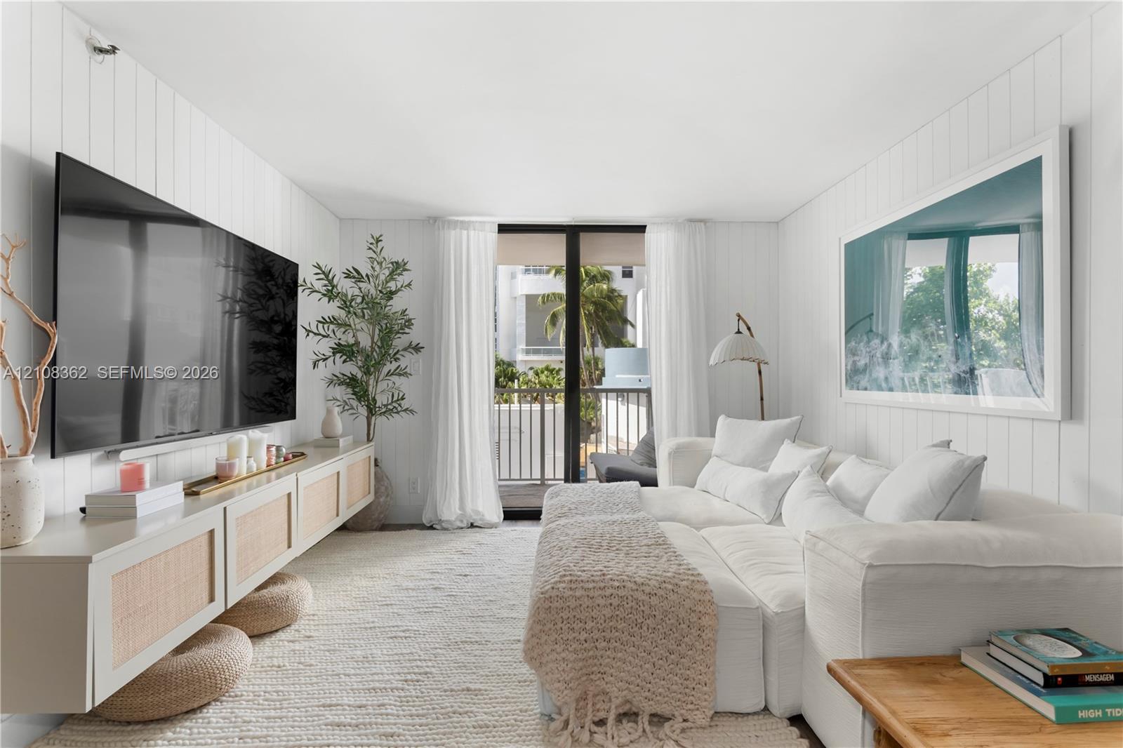 Living area featuring vertical plank wall paneling, a wall-mounted built-in console with cane detailing, and glass sliding doors leading to an exterior balcony